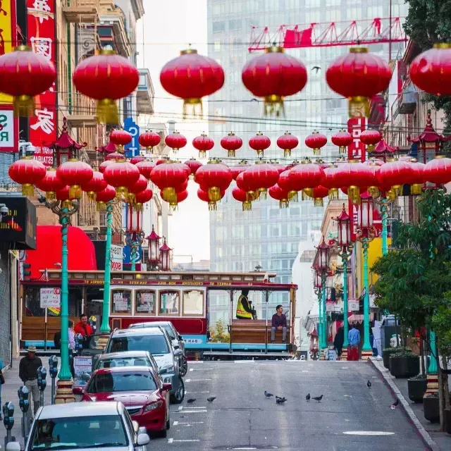 Una strada collinare nella 唐人街 di San Francisco è raffigurata con lanterne rosse penzolanti e un tram che passa.